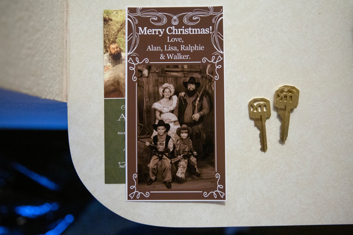 A Christmas card lays next to a pair of bronze keys. On the card, a woman, man and two young boys are dressed in costumes from the Old West.