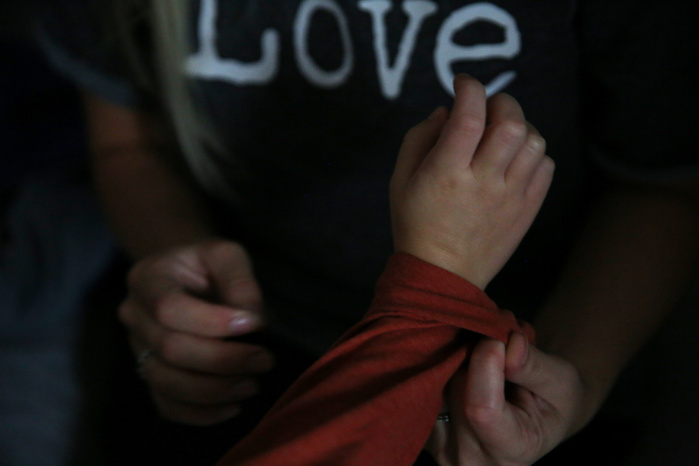 A woman's hands help adjust the sleeve of a child. Behind the child's hand, the woman's shirt says "Love."