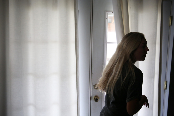A silhouetted woman looks away from a set of white curtains.