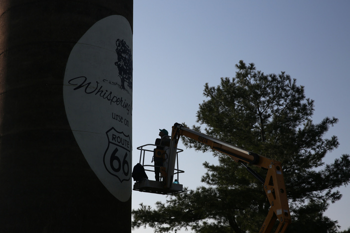 A silhouetted woman operates a boom lift while looking up at a grain silo.