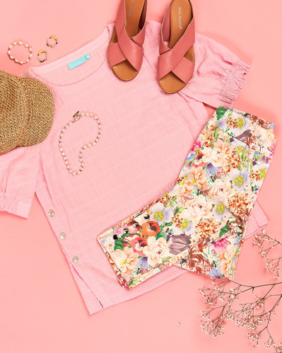 a flatlay of pink shirt, colourful flowery pants and pink shoes on a pink background