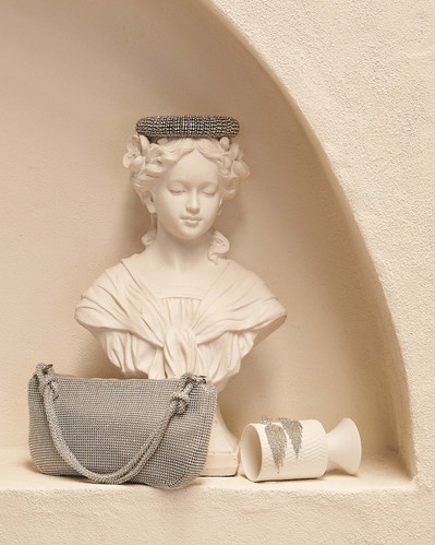 silver bag and silver earrings propped on a white statue