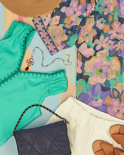 a flatlay of floral blouse, green blouse, white pants