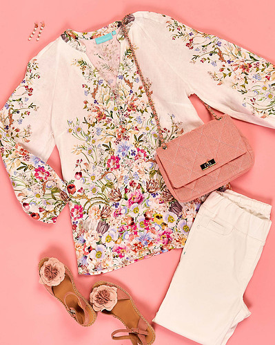 a flatly of floral blouse, white pants and accessories on a pink background