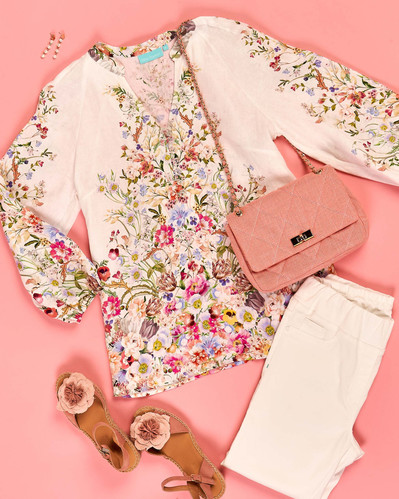 a flatly of floral blouse, white pants and accessories on a pink background