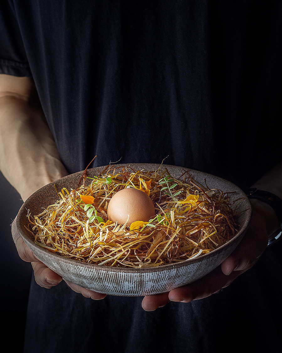 hands holding a brunch dish with an egg in the centre of the plate