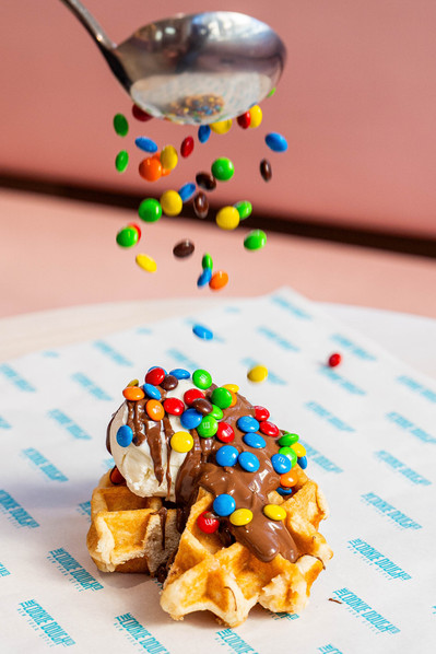 chocolate drops being dropped on a waffle with ice cream on top