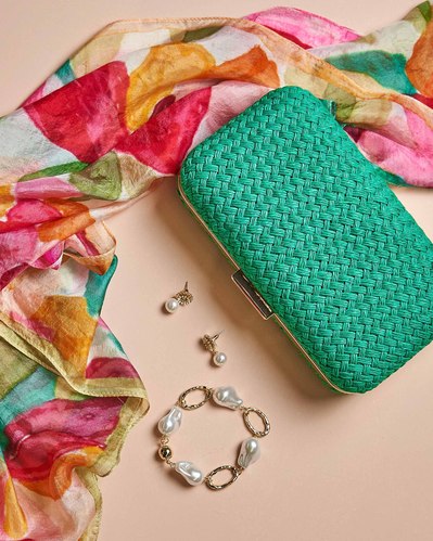green bag and a floral colourful scarf and jewelry on a beige background