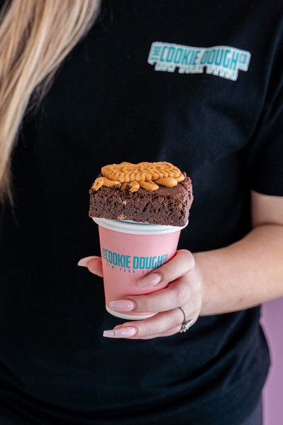 a hand holding a pink take away coffee cup with a brownie on top