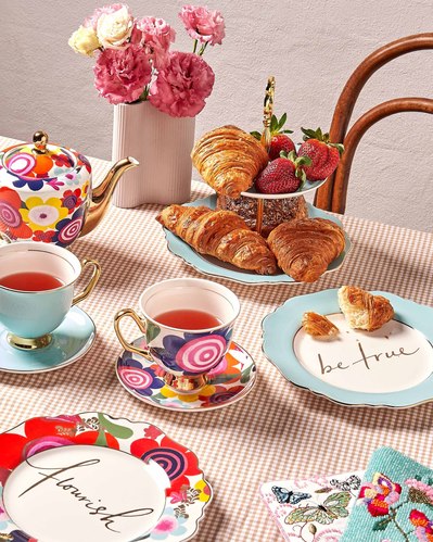 high tea set with cute colourful plates and sweets on them as well as two tea cups and fresh flowers in a vase