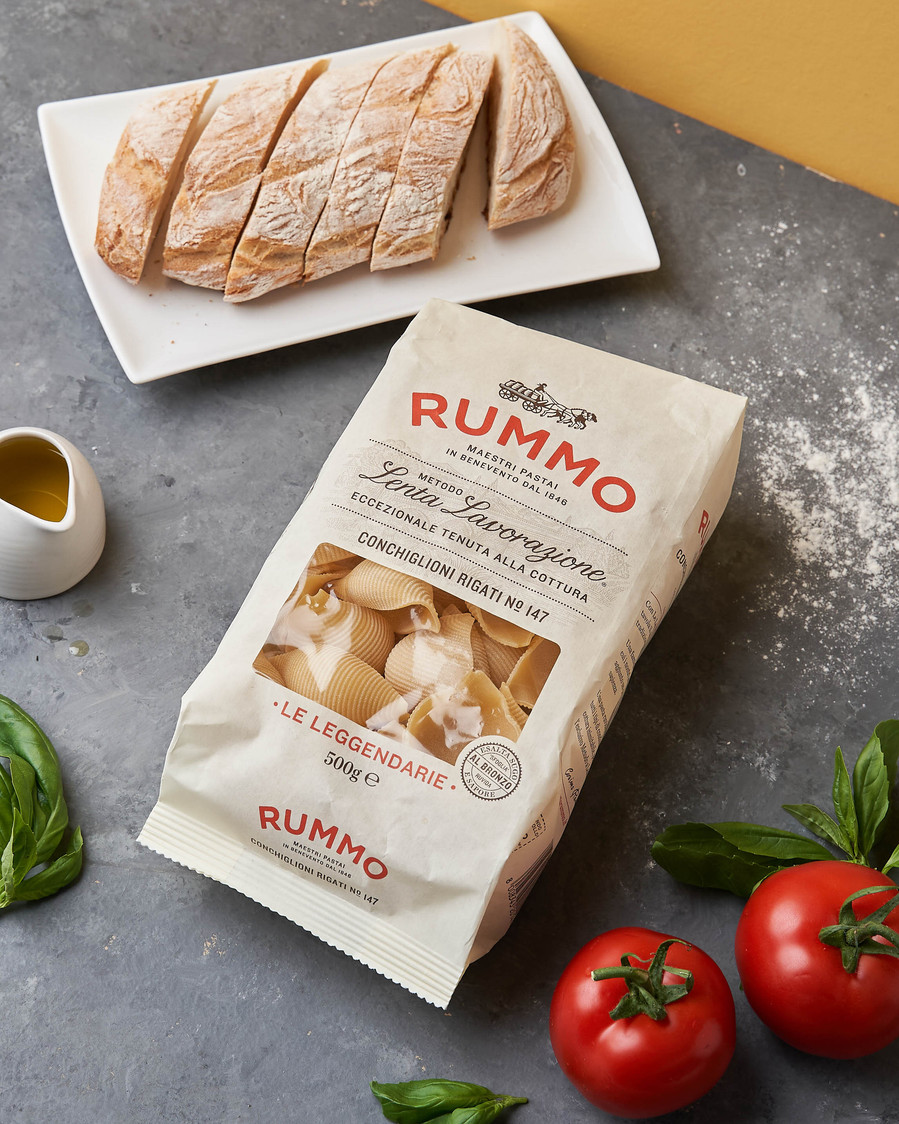 Rummo pasta bag styled with sliced ciabatta, basil, tomatoes, and olive oil on a stone surface