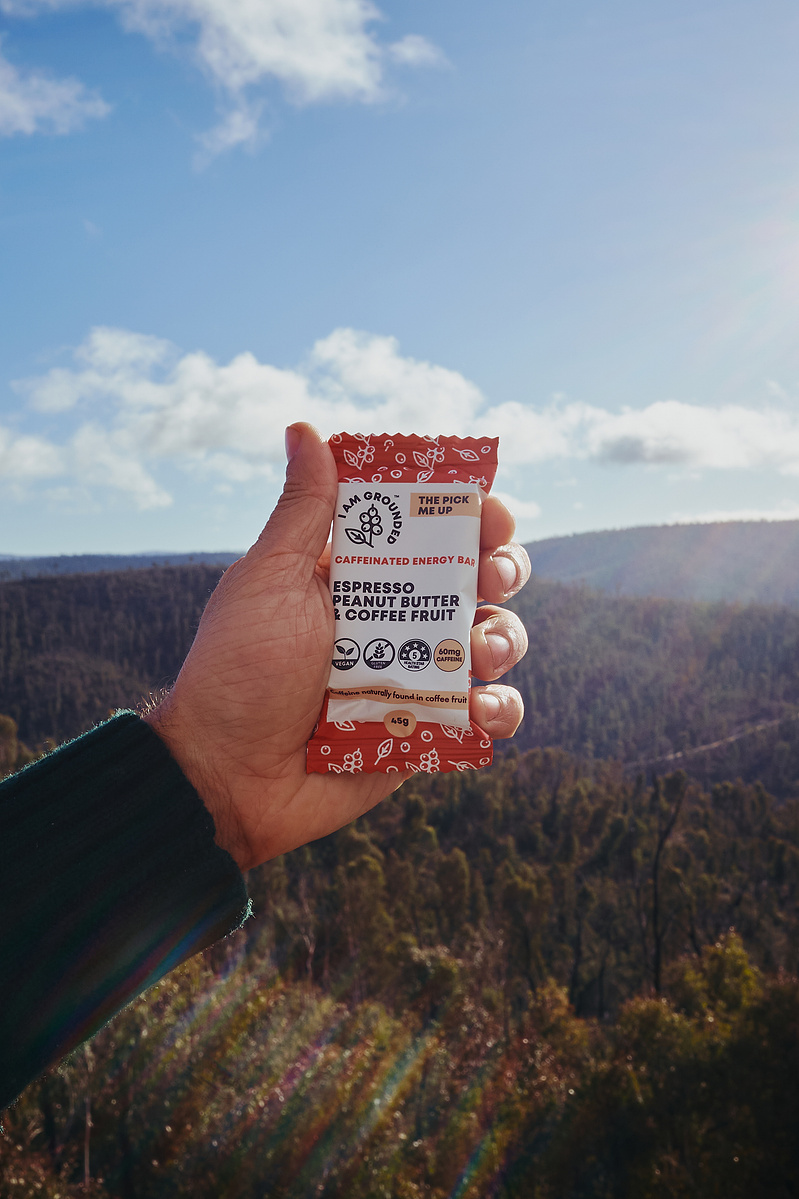 Hand holding an energy bar with forest and mountains in background — outdoor product photography Melbourne