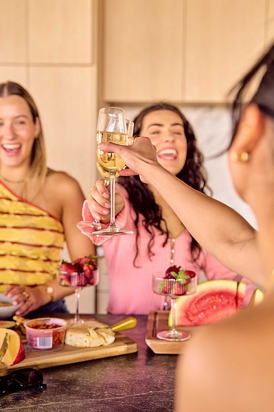 Friends laughing while pouring wine at indoor picnic – Melbourne lifestyle content by Marcie Raw