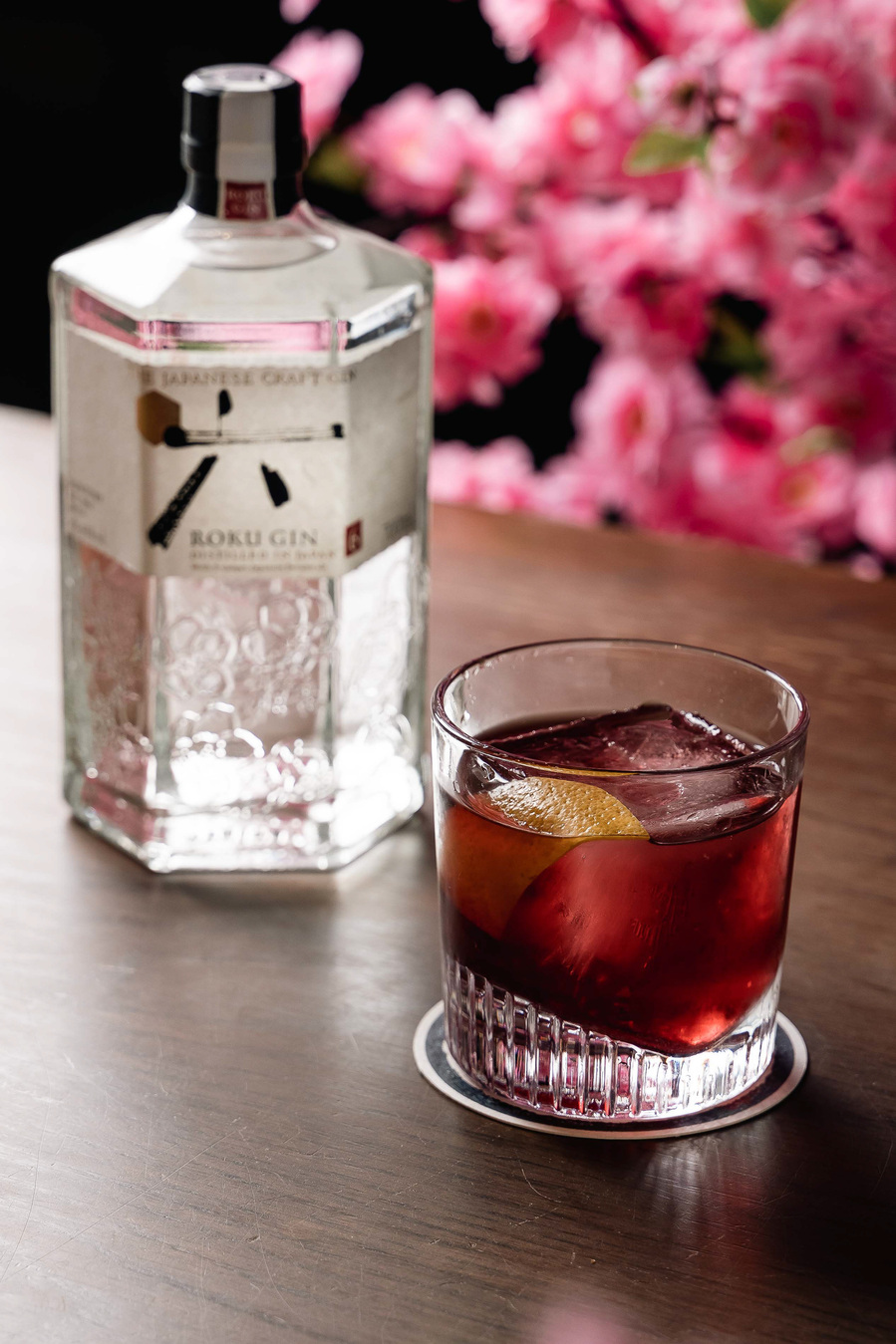 Gin and negroni cocktail styled with cherry blossom branches on a sleek bar surface