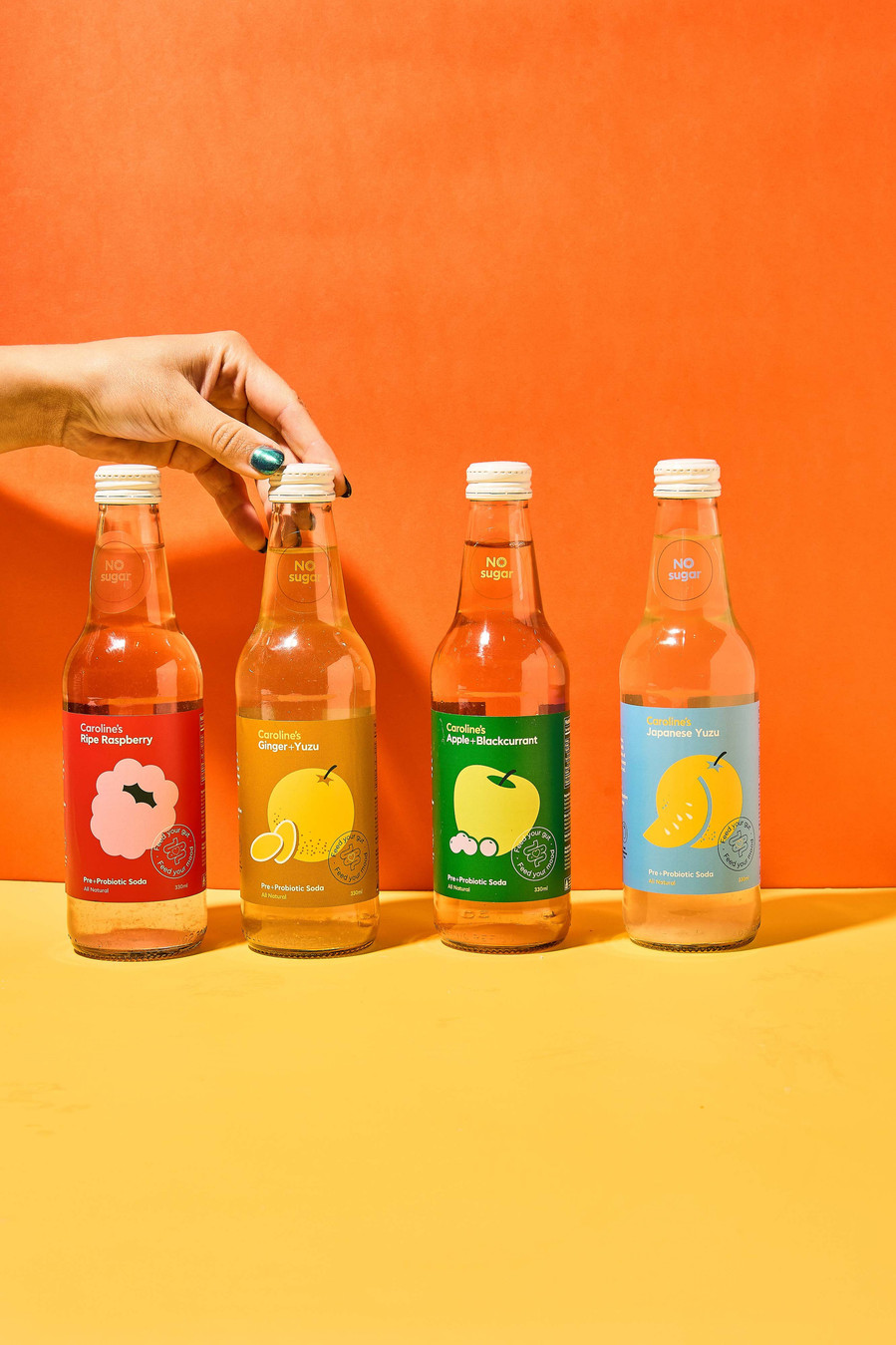 four kombuchas in a row with a hand coming from the right side and reaching for one kombucha