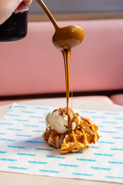 a hand pouring liquid peanut butter on a sweet waffle with ice cream on top