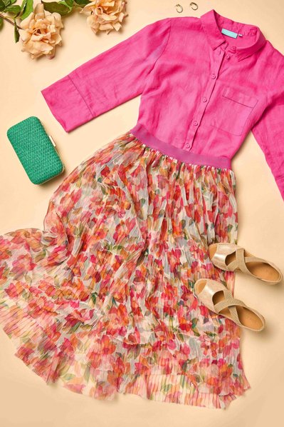 a flatlay of pink shirt, floral maxi skirt a and a green bag  on a beige background