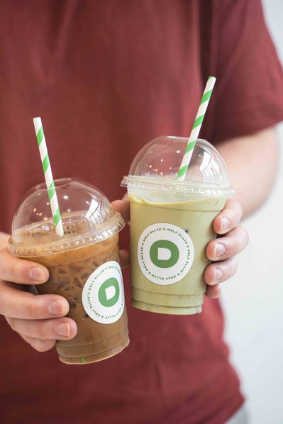 a man holding two iced drinks - iced coffee and iced matcha