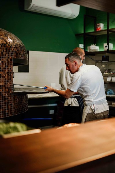 a pizza maker taking the pizza out of the oven
