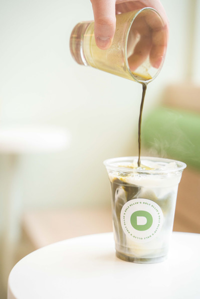a hand pouring matcha into a glass of milk