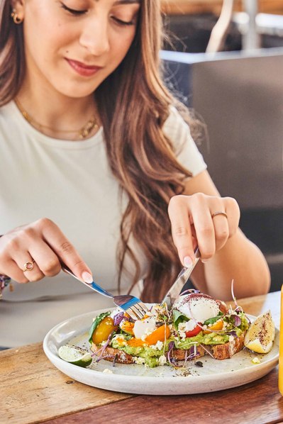 a young girl sitting at a cafe and eating avocado on toast
