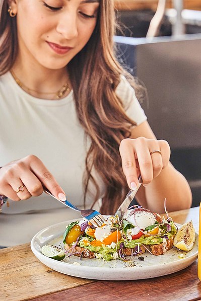 a young girl sitting at a cafe and eating avocado on toast