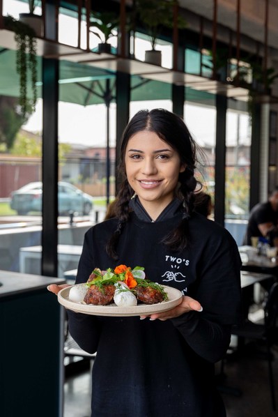 a young pretty girl holding a brunch item and smiling at the camera in front of a cafe