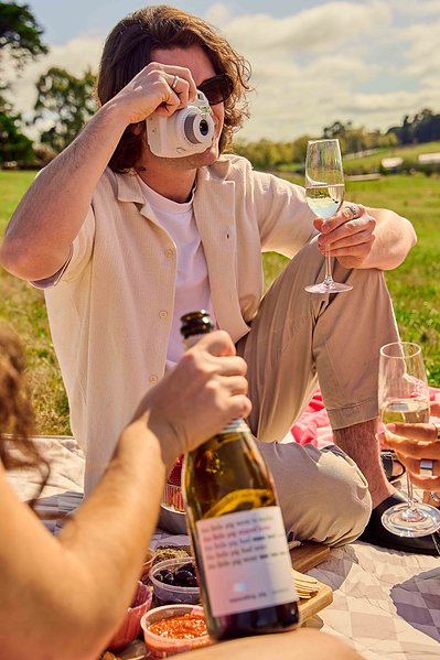 Man taking polaroid photo with glass of sparkling wine – relaxed picnic moment by Melbourne photographer Marcie Raw