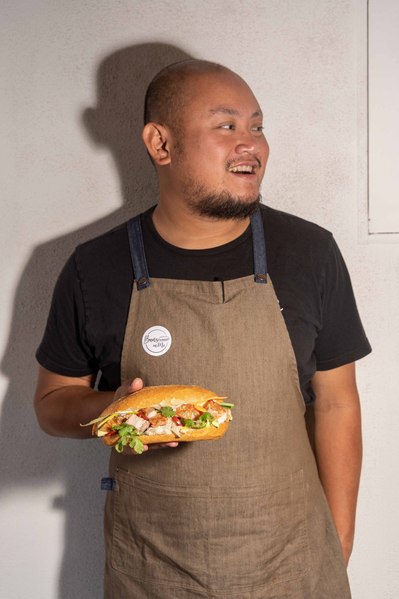a chef holding banh mi he's made and smiling