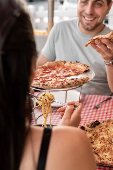 a handsome boy eating a pizza and looking at a girl with whom he's sitting at the table
