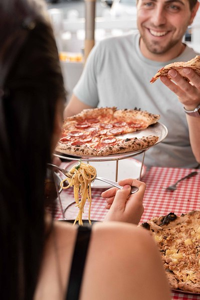 a handsome boy eating a pizza and looking at a girl with whom he's sitting at the table