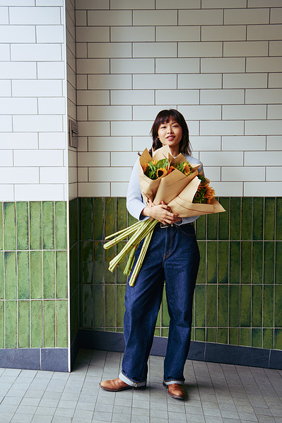 Woman holding flower bouquets and smiling in front of tiled wall, captured by Melbourne lifestyle photographer Marcie Raw