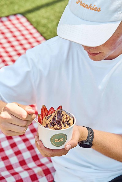 Person enjoying an acai bowl topped with strawberries and chocolate drizzle at a picnic in Melbourne