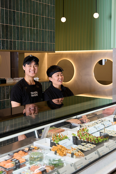 Two staff members smiling behind a counter at a modern sushi restaurant called Sushi Sushi  in Melbourne