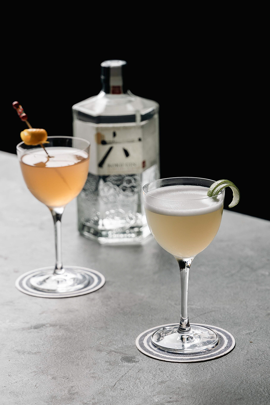 Elegant gin-based cocktails in coupe glasses with garnishes, set against dramatic black background