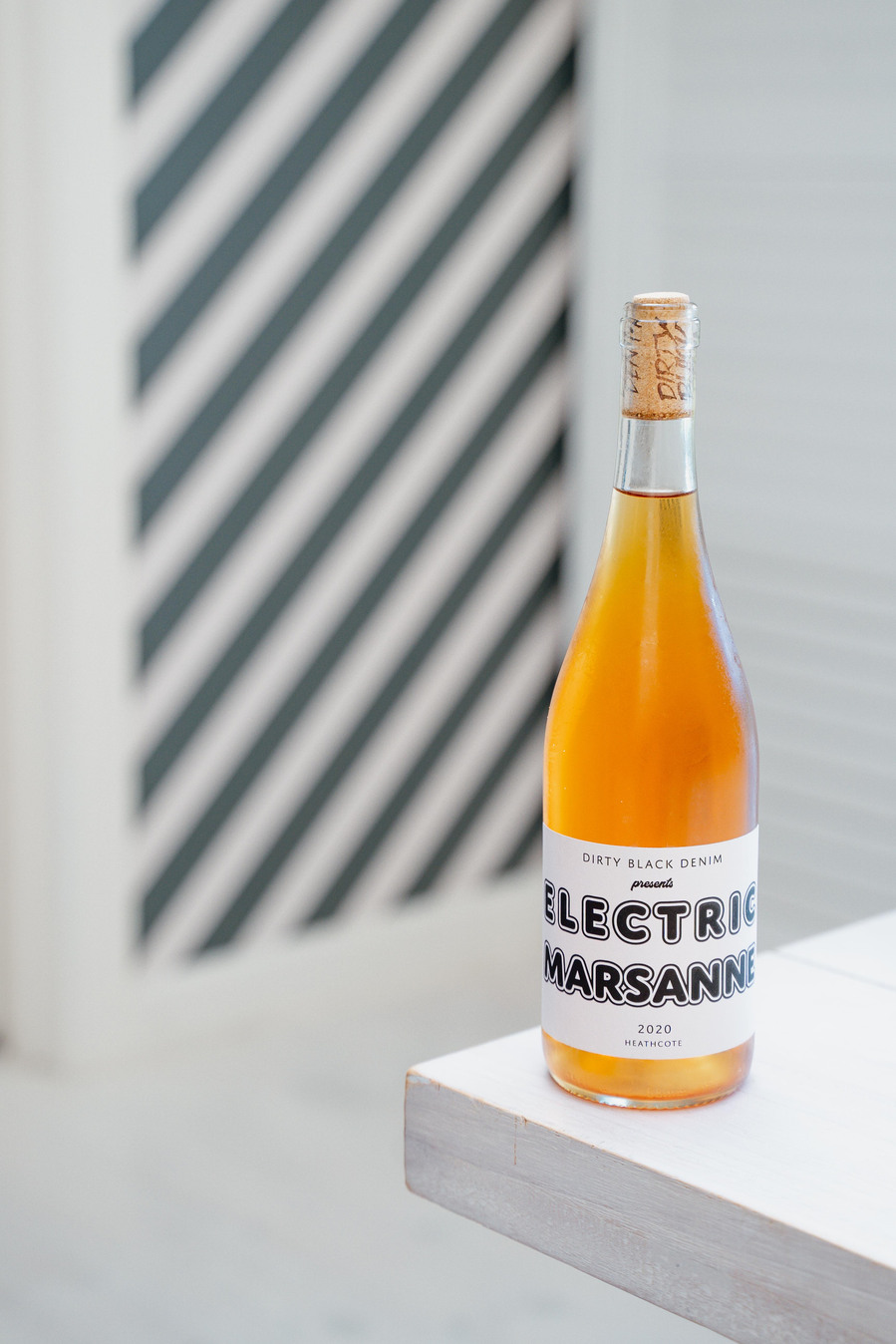 orange wine sitting on the edge of a white table with a striped wallpaper in the background