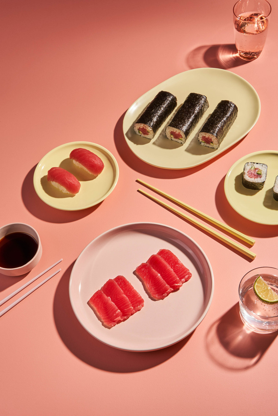 Colorful sushi platter including nigiri and maki rolls styled on pastel yellow plates and pink background
