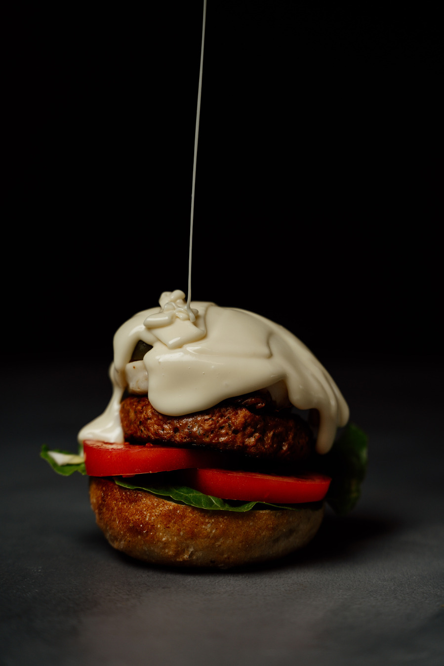 a big burger in the centre of the frame with sauce being poured onto it