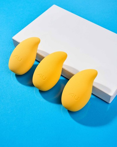 three yellow make up brushes lying against a white plinth