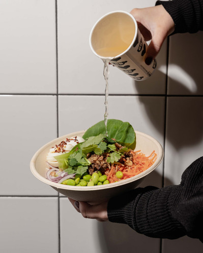 hands pouring a broth to a noodle salad