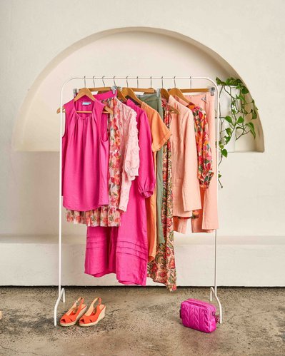 a collection of pink and beige shirts, pants and dresses on a white metal clothing rack