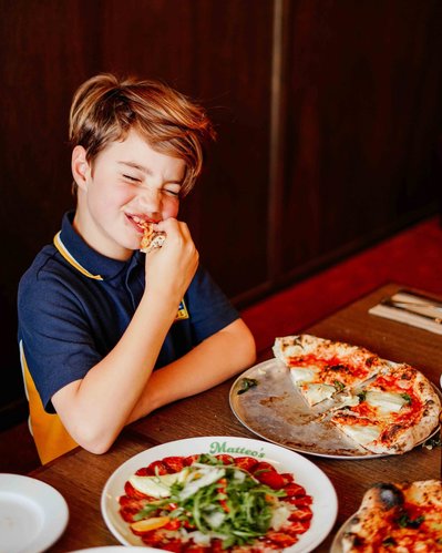 a boy eating a pizza slice in a restaurant and laughing