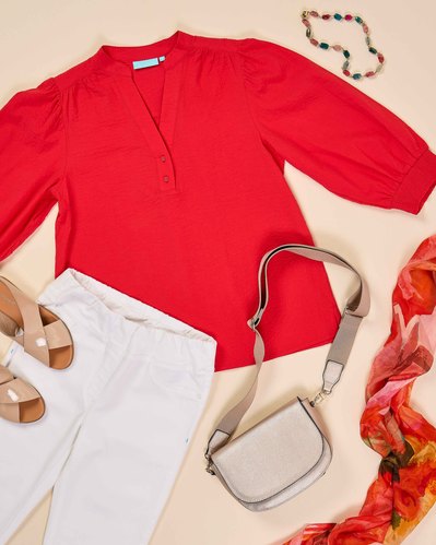 a flatlay of red blouse, white pants and tan espadrilles and a colourful scarf  on a beige background