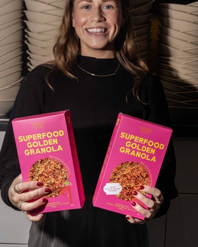a young girl holding two big granola boxes smiling