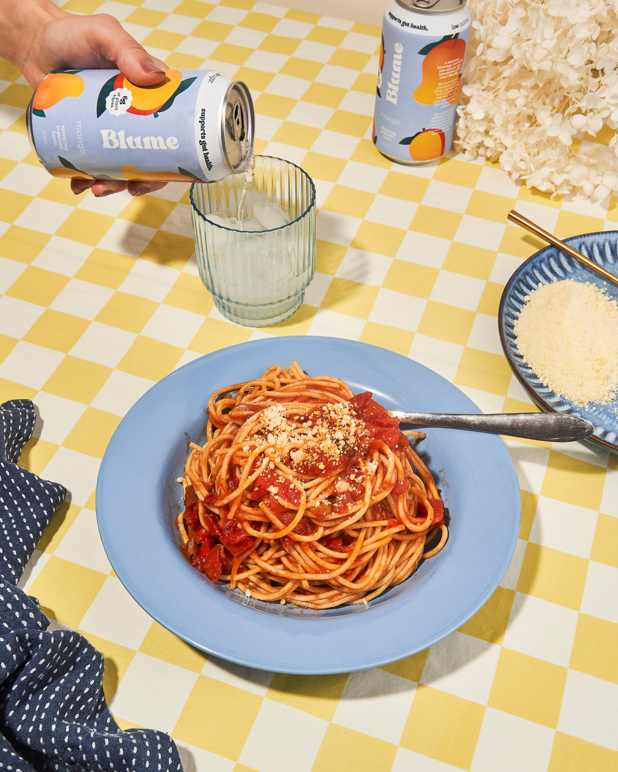 spaghetti bolognese in a blue bowl placed on a checkered yellow and white table cloth 