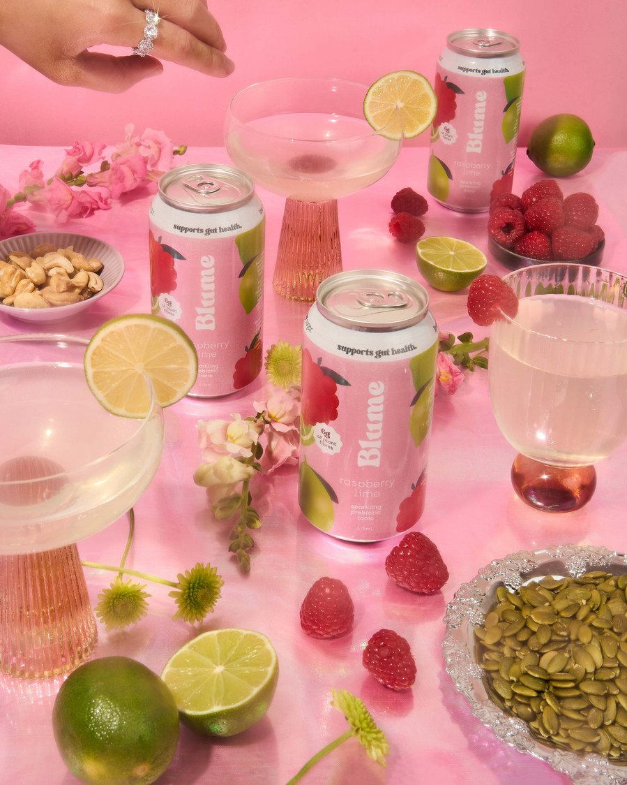 a spread with kombucha cans, fresh limes, raspberries and flowers on a table 