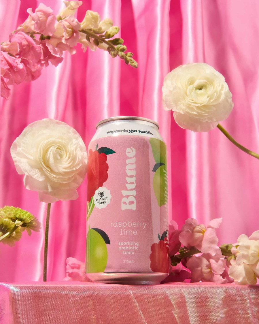 a can of kombucha surrounded by flowers on a pink backdrop