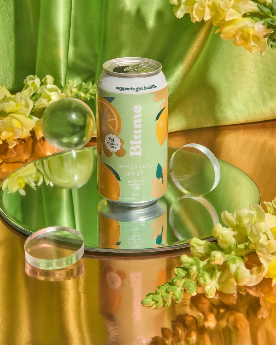 kombucha in a green can lying on top of the mirror surrounded by yellow flowers