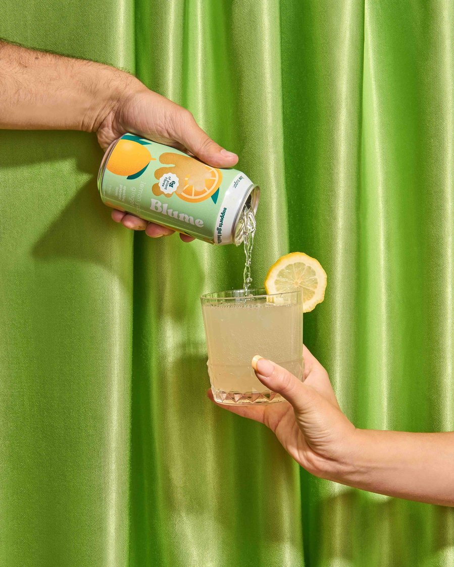 a hand pouring a kombucha from a can to a glass