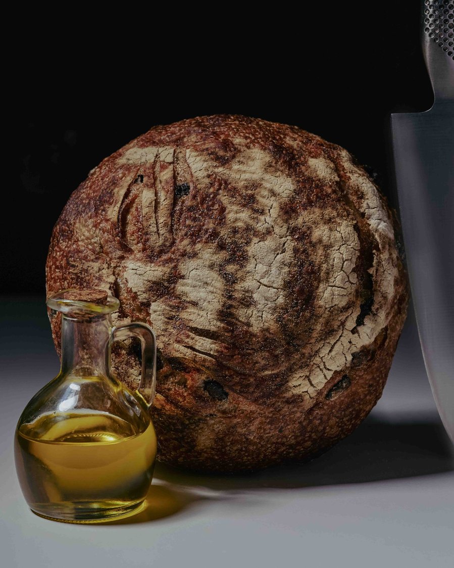 Loaf of artisan bread with a small glass jug of olive oil on a black and white background